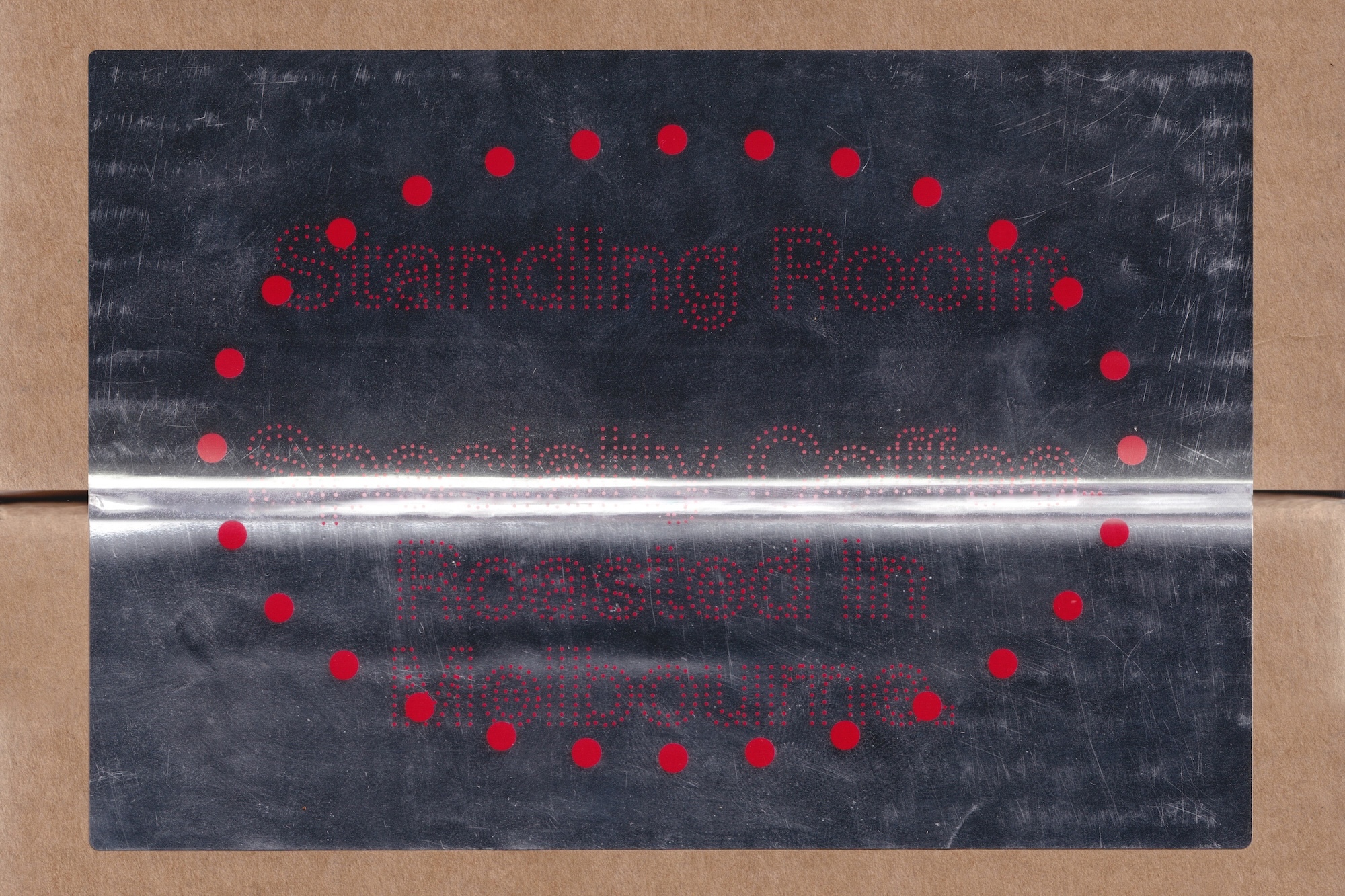Metallic brand label with red dotted typography affixed to a brown cardboard surface