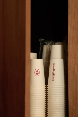 Stacks of white disposable paper coffee cups with red branding inside a wooden cabinet