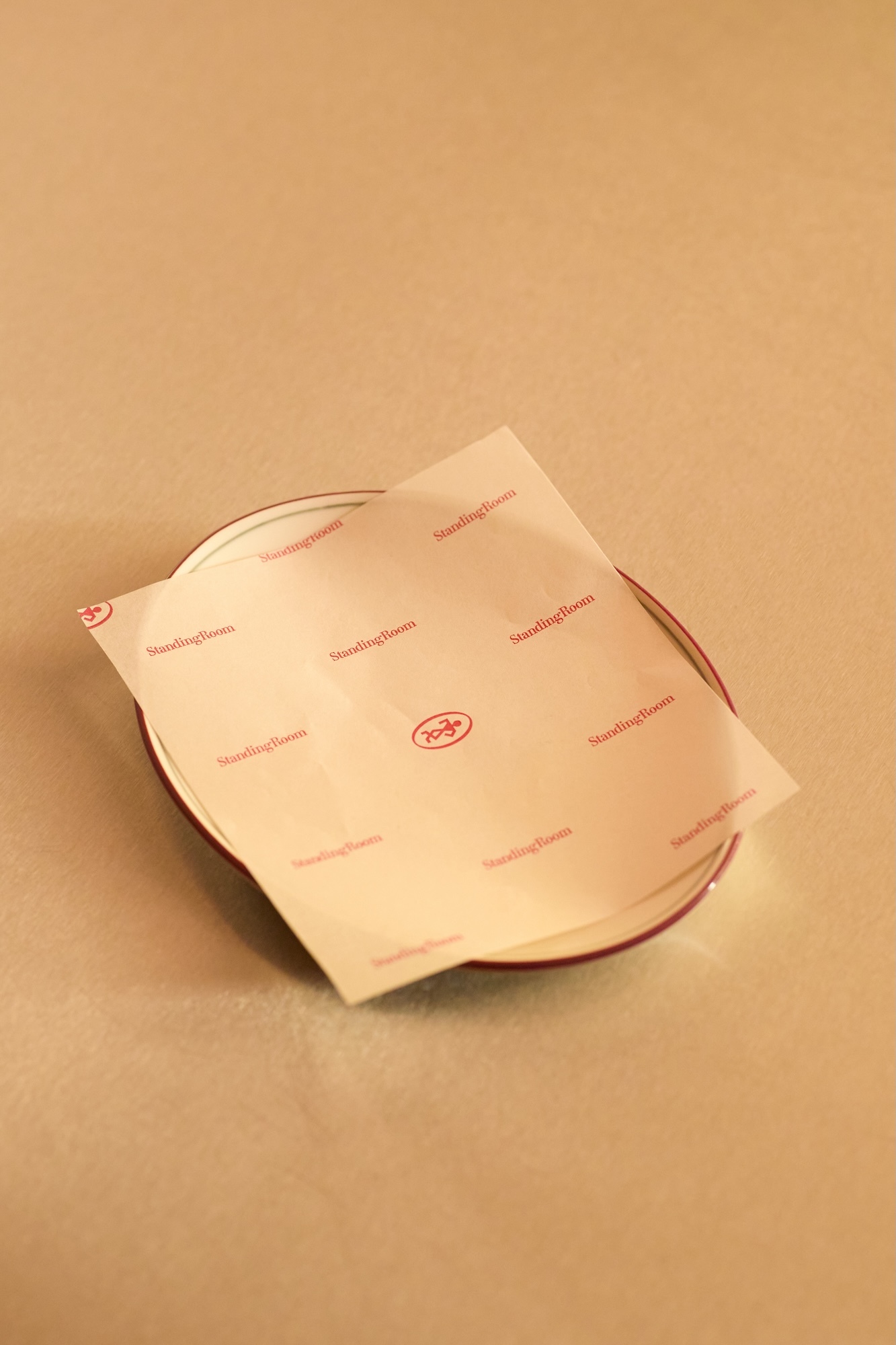 Printed wax paper resting on a small ceramic saucer against a neutral beige background