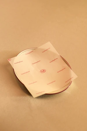 Printed wax paper resting on a small ceramic saucer against a neutral beige background