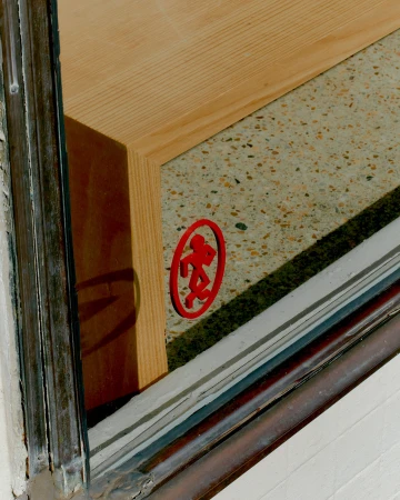 Close-up of a wooden display structure and a red circular logo behind a glass window frame.