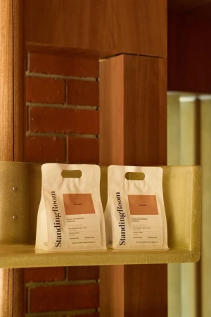 Two white coffee bags with printed labels resting on a pale shelf against a red brick and wood interior wall