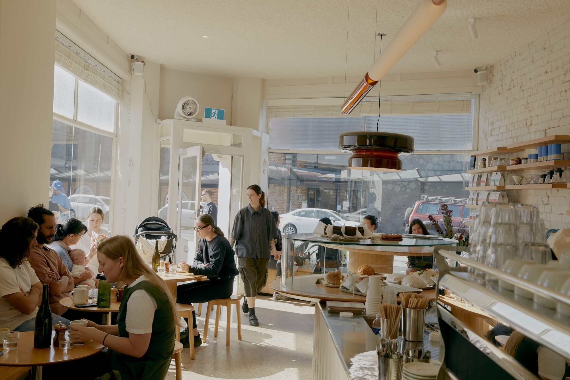 Interior view of Standing Room cafe with patrons seated at wooden tables, a staff member walking through, and a counter in the foreground