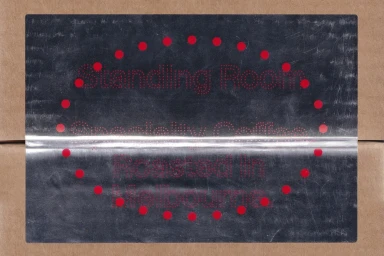 Metallic brand label with red dotted typography affixed to a brown cardboard surface