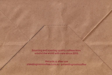 Brown craft paper texture with creased folds and printed red text detailing coffee sourcing and recycling info.