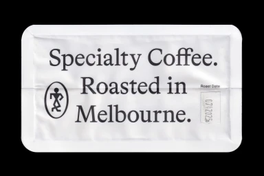 White specialty coffee packaging pouch with bold black typography reading Specialty Coffee Roasted in Melbourne against a black background