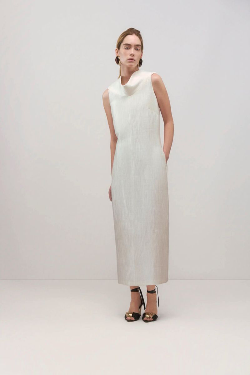 Full-length shot of a woman in a sleeveless white dress with high-heeled sandals in a bright studio setting.