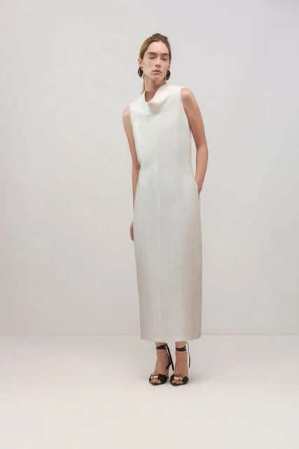 Full-length shot of a woman in a sleeveless white dress with high-heeled sandals in a bright studio setting.