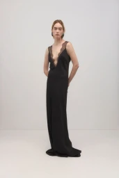 A model standing against a light background wearing a long black evening dress with lace trim.