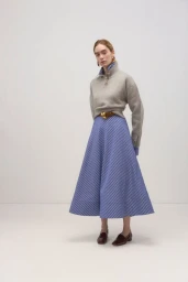 Model in grey high-neck sweater and blue striped skirt against a seamless white studio background