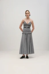 Model standing against a white seamless background wearing a patterned midi dress with a black belt and dark loafers.