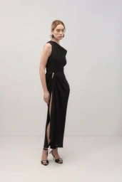 Model wearing a black sleeveless dress and strappy heels standing against a neutral white background