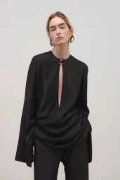 Model wearing a black keyhole blouse and gold statement earrings against a neutral grey studio background