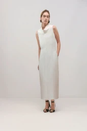 Model wearing a sleeveless cream midi dress and black strapped heels against a minimalist light grey studio background.