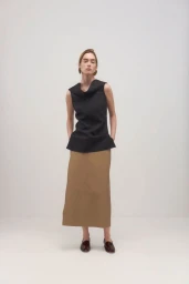 Model standing against a white seamless backdrop wearing a black sleeveless top and tan skirt.