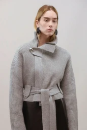 Model wearing a grey ribbed sweater with high collar and belted waist against a neutral background for Brandon Maxwell lookbook