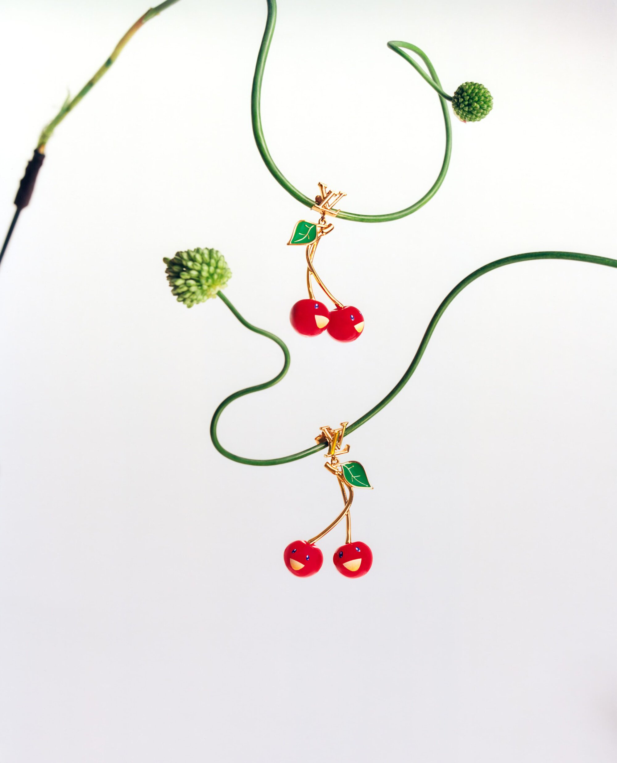 Two Louis Vuitton cherry bag charms hanging on curved green stems against a plain white background.