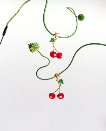 Two Louis Vuitton cherry bag charms hanging on curved green stems against a plain white background.