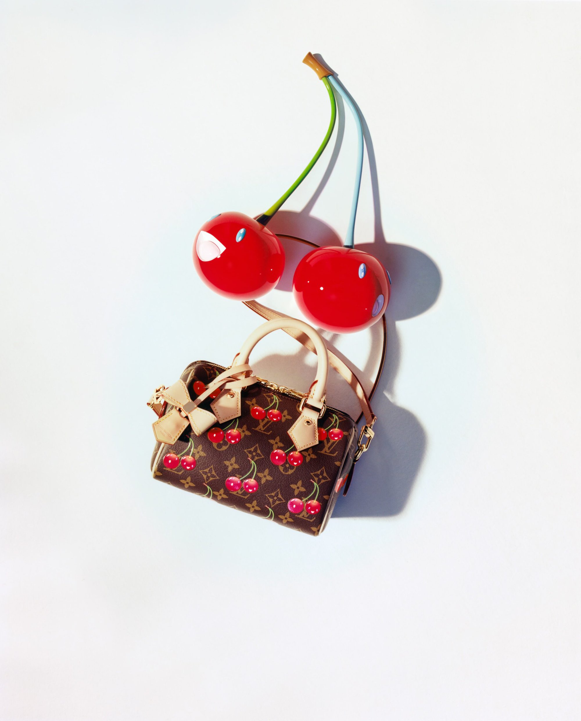 Louis Vuitton x Murakami cherry print handbag with large sculptural red cherry props against a white background