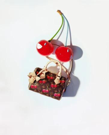Louis Vuitton x Murakami cherry print handbag with large sculptural red cherry props against a white background