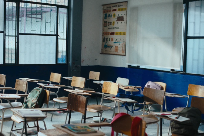 Empty school classroom with wooden desks and chairs, large windows, and a poster on the wall