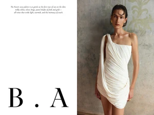 Model wearing a white draped one-shoulder dress with gold earrings against an ornate patterned wall