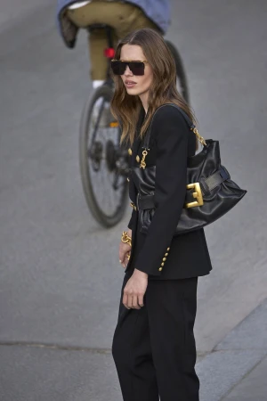 Woman in a black blazer wearing sunglasses and carrying a black handbag outdoors
