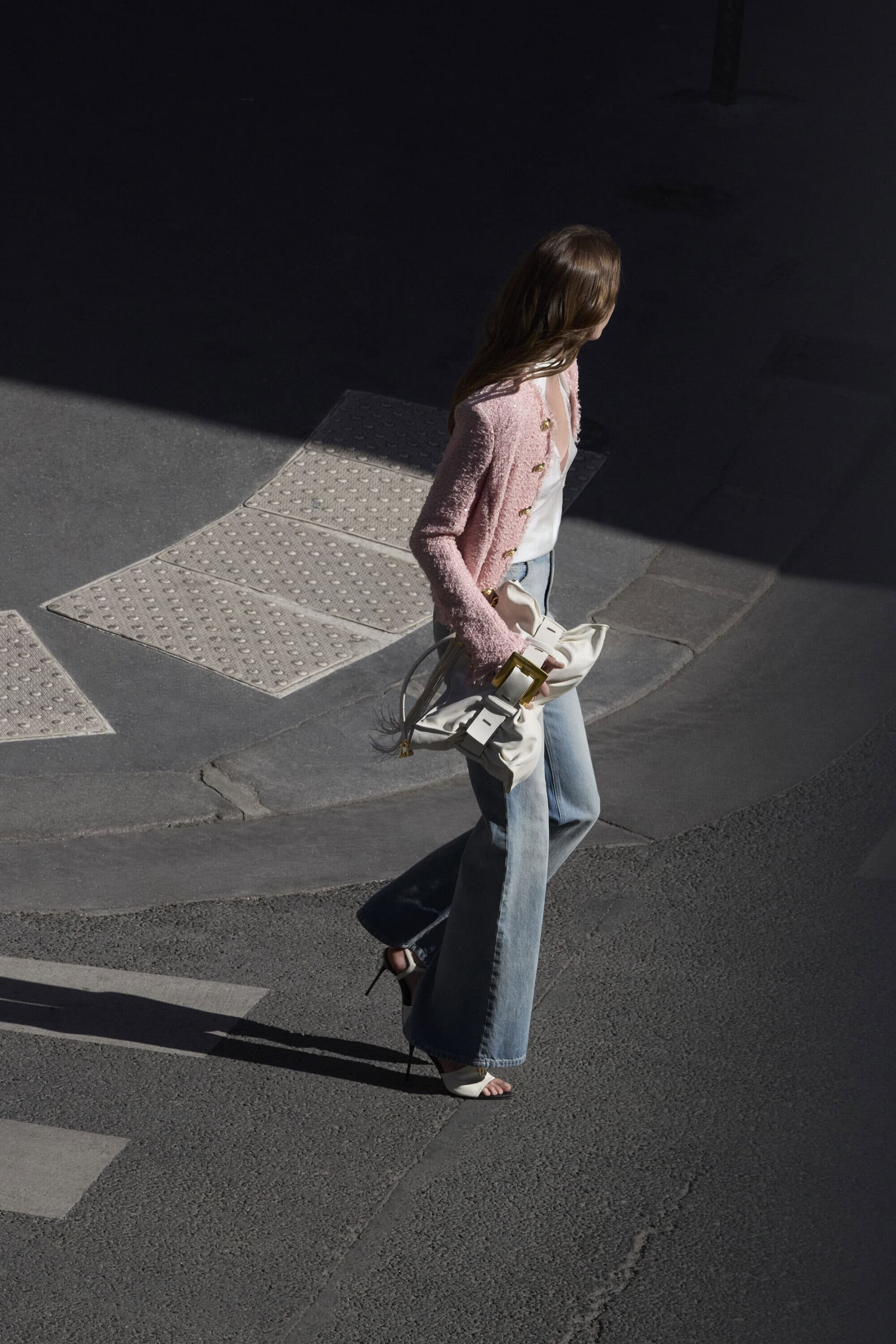 Model in pink tweed jacket and flared jeans walking outdoors with white shoulder bag