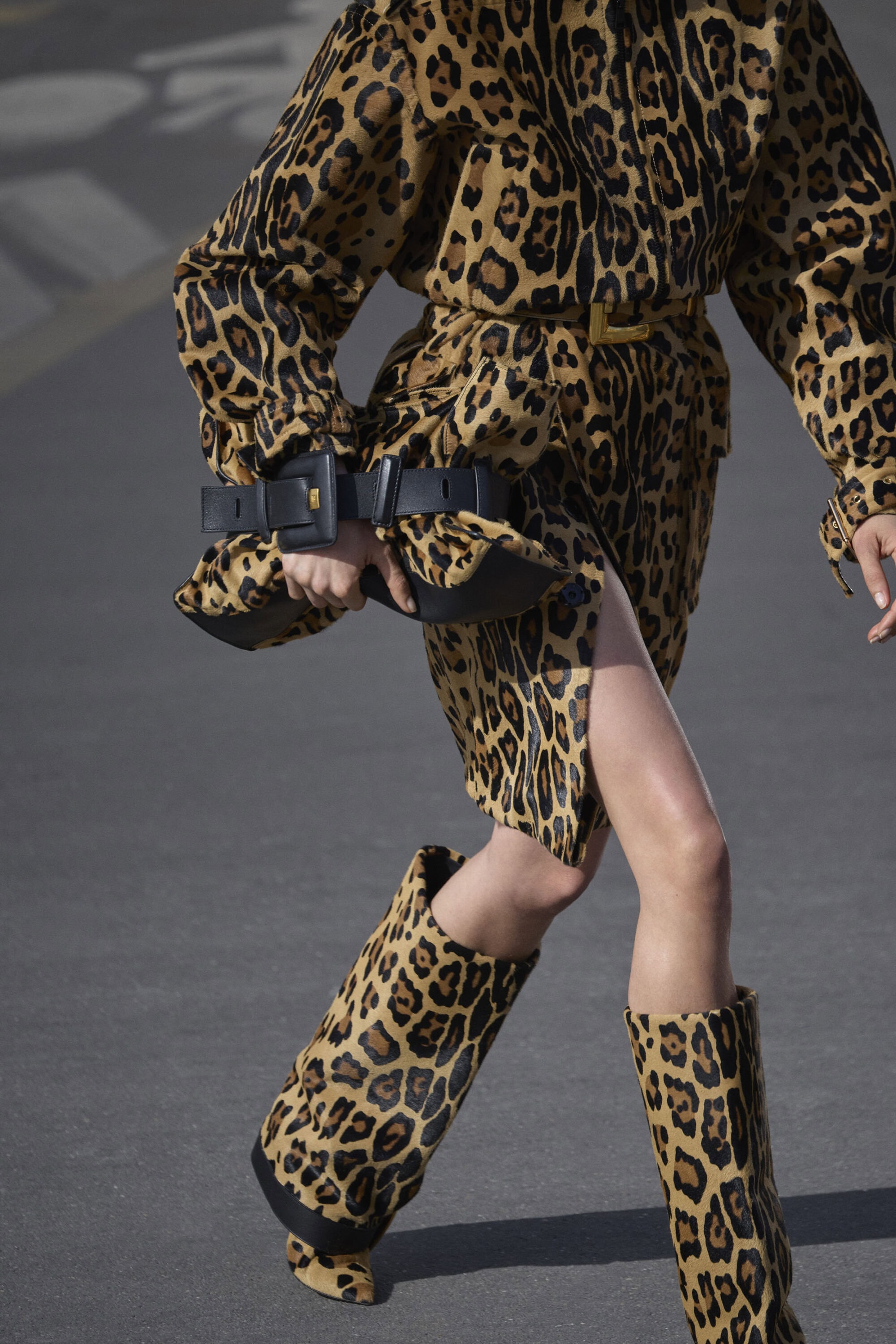 Model wearing a matching leopard print outfit and boots carrying a black handbag against a grey background