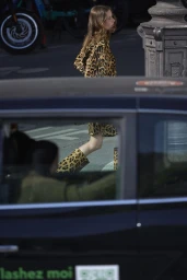 Woman in leopard print coat and boots walking past a car window in an urban street setting.