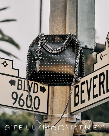 Black studded handbag with chain strap resting on a street sign pole in Los Angeles for Stella McCartney