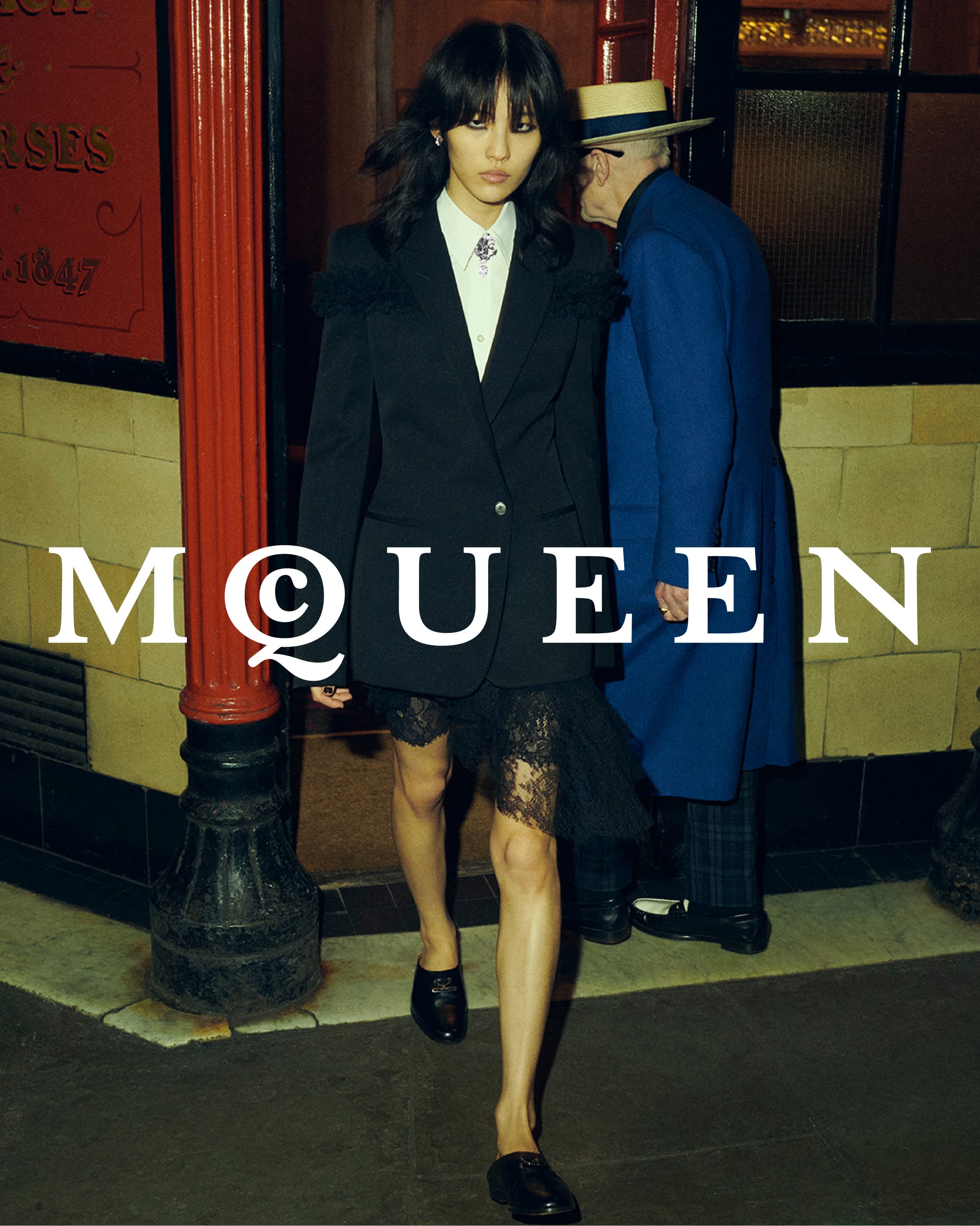 Model in black blazer and lace skirt walking past a pub entrance in London
