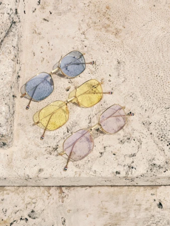 Three pairs of tinted designer sunglasses with gold frames displayed diagonally on a weathered stone surface.
