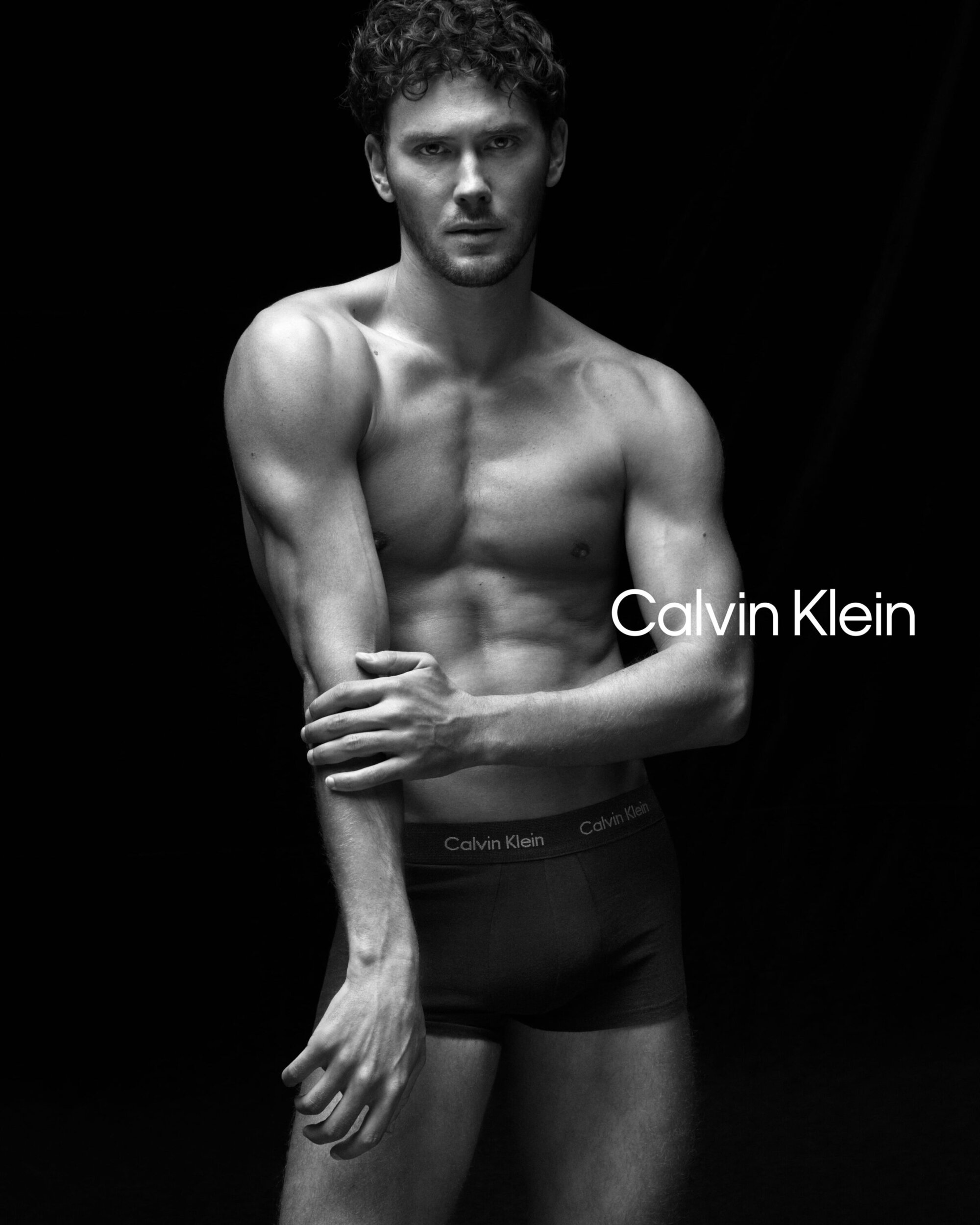 Cooper Koch posing shirtless in dark underwear against a black background for Calvin Klein ad campaign