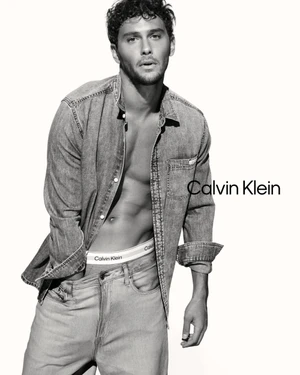 Cooper Koch posing in an unbuttoned denim shirt and jeans against a white seamless background for Calvin Klein.