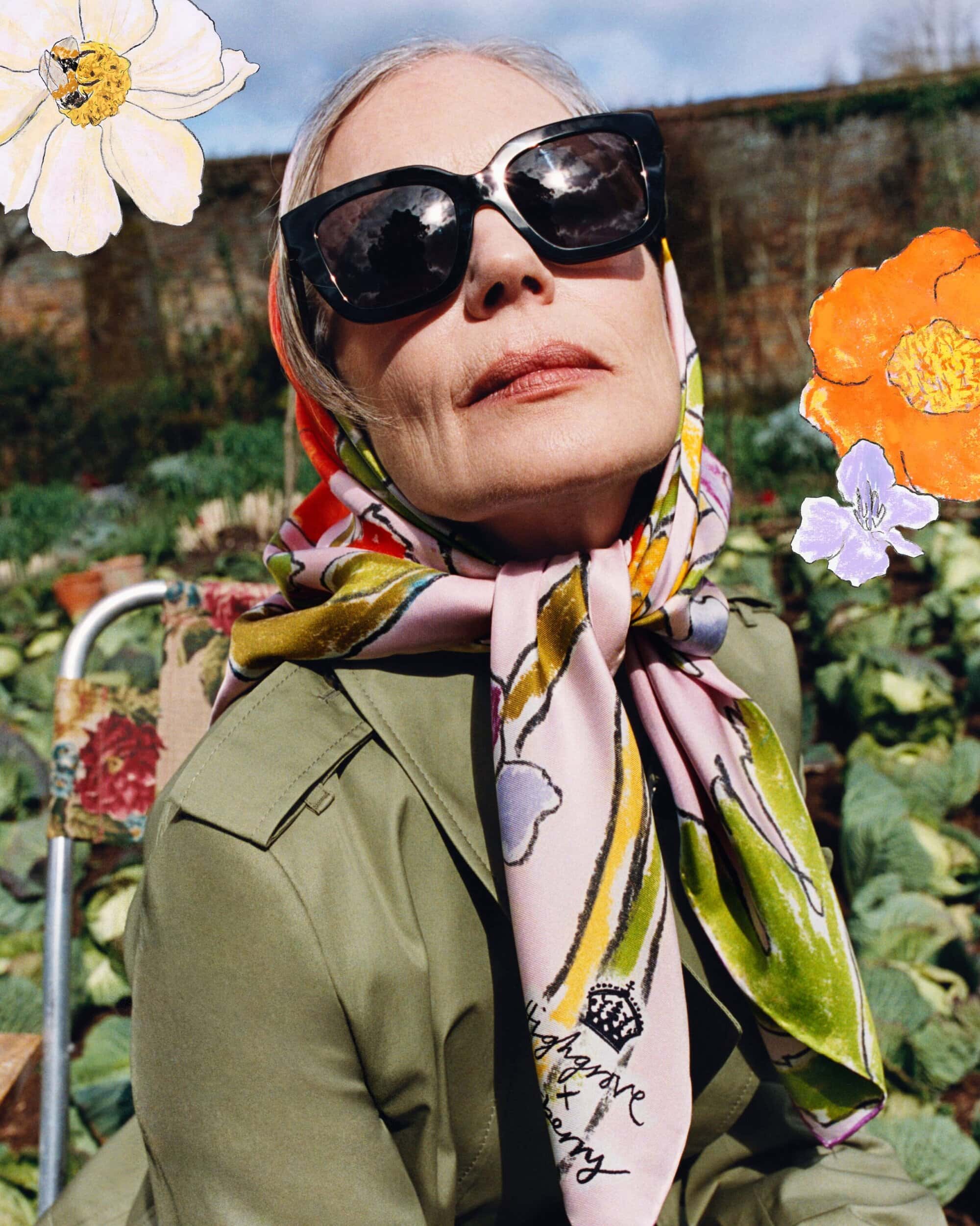 Model wearing dark sunglasses and a patterned silk headscarf with an olive green coat outdoors in a garden