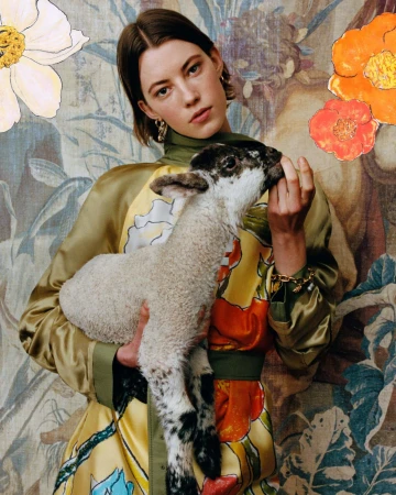 Model holding a young lamb against a botanical tapestry backdrop for Burberry