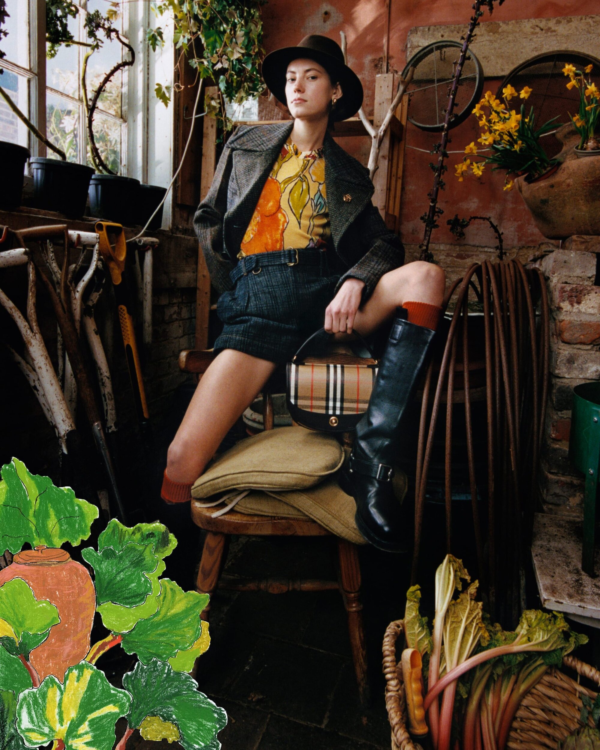 Model wearing a fedora hat, patterned top, and dark jacket while seated on a wooden chair in a rustic greenhouse setting.