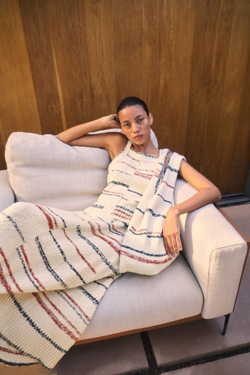 A woman rests on a cream-colored sofa in a patterned sweater dress, next to a light-colored wooden wall inside a modern home.