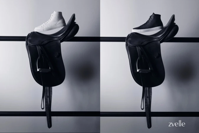 High-top sneakers resting on leather saddles mounted on a dark horizontal rail against a neutral grey wall.