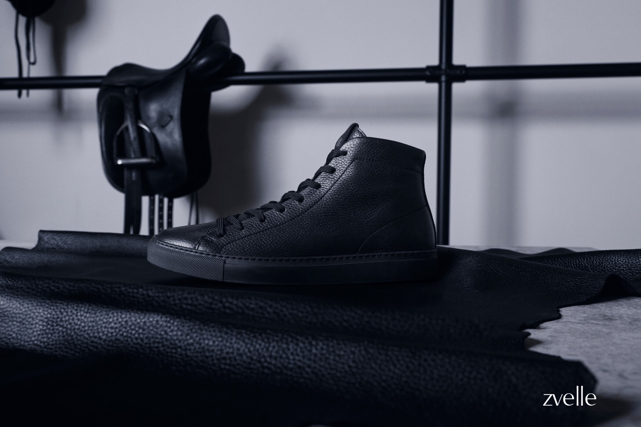 Black leather high-top sneaker resting on black hide with a saddle hanging in the background for Zvelle