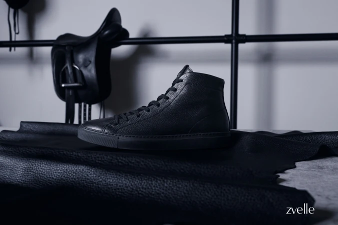 Black leather high-top sneaker resting on black hide with a saddle hanging in the background for Zvelle