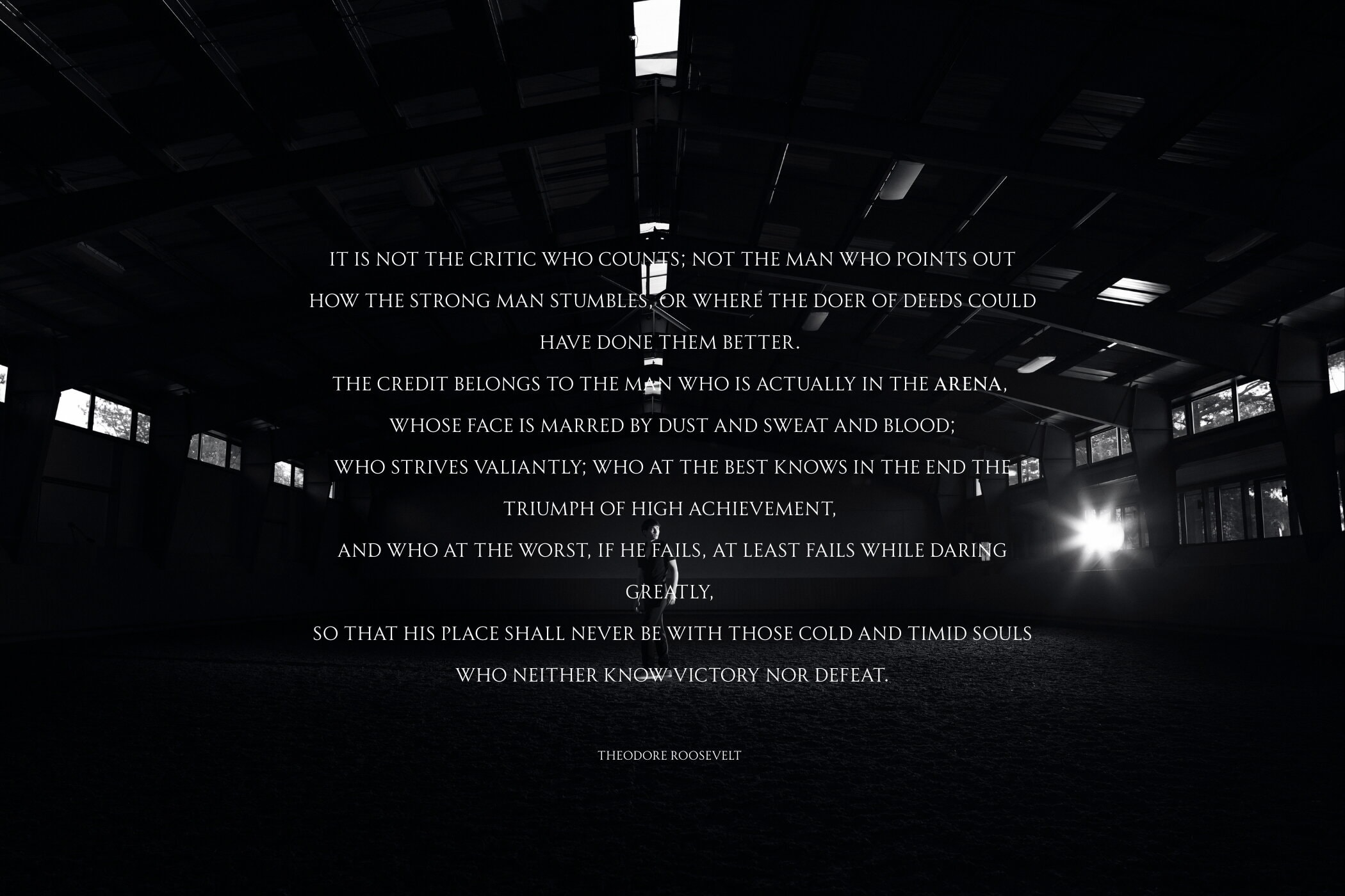 Man standing in the center of a dark indoor riding arena with overlaid white text from Theodore Roosevelt's speech.