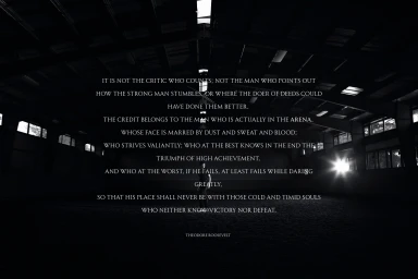 Man standing in the center of a dark indoor riding arena with overlaid white text from Theodore Roosevelt's speech.