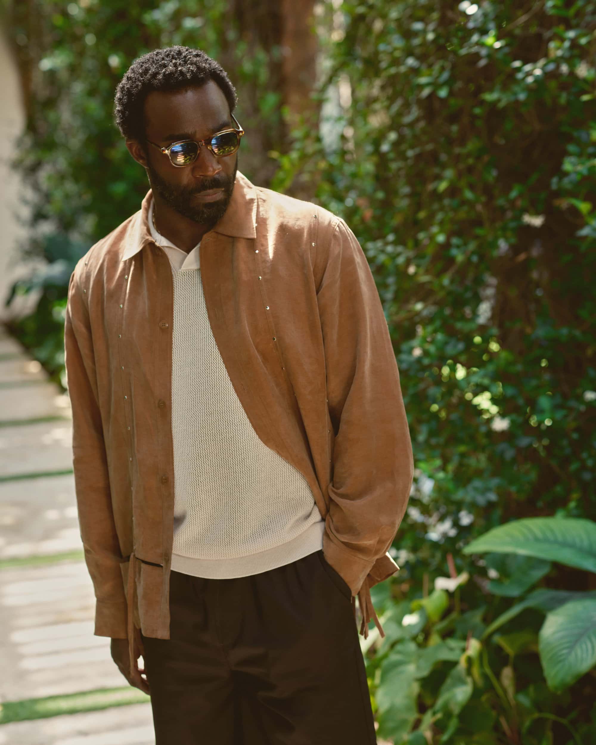 Tramell Tillman wearing brown suede shirt and sunglasses outdoors for Kith Spring 2025 ad campaign.