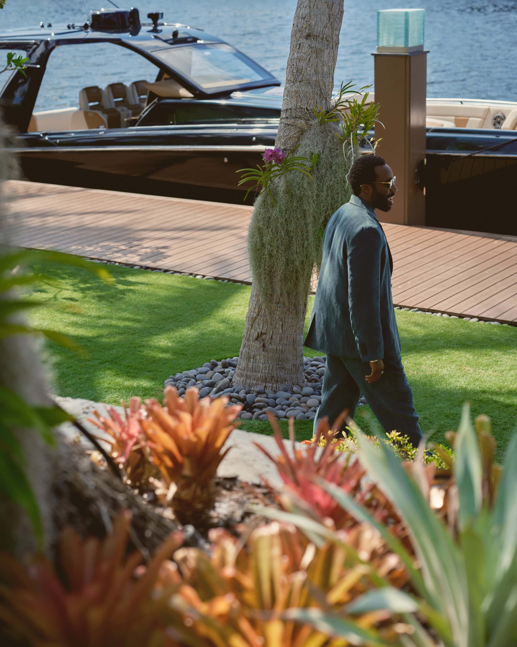 Tramell Tillman walking near a dock and a luxury boat wearing a dark suit for Kith