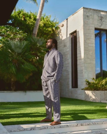 Tramell Tillman wearing a patterned suit standing outside a modern stone house for Kith Spring 2025 campaign