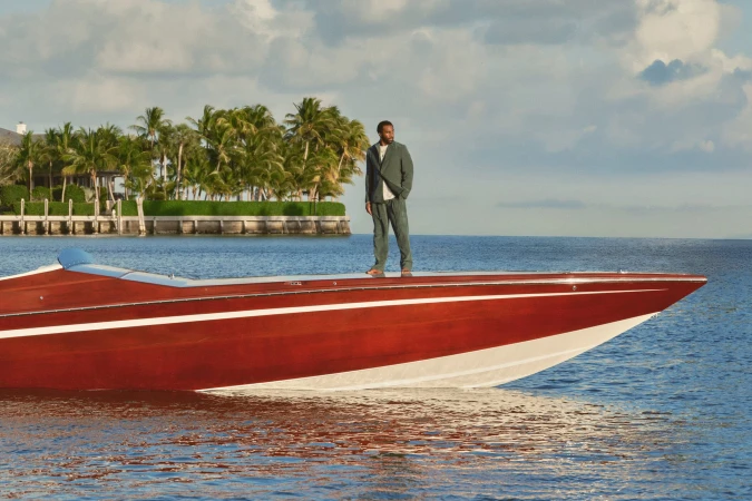 Tramell Tillman standing on the deck of a classic wooden motorboat on the water for Kith Spring 2025 Ad Campaign.