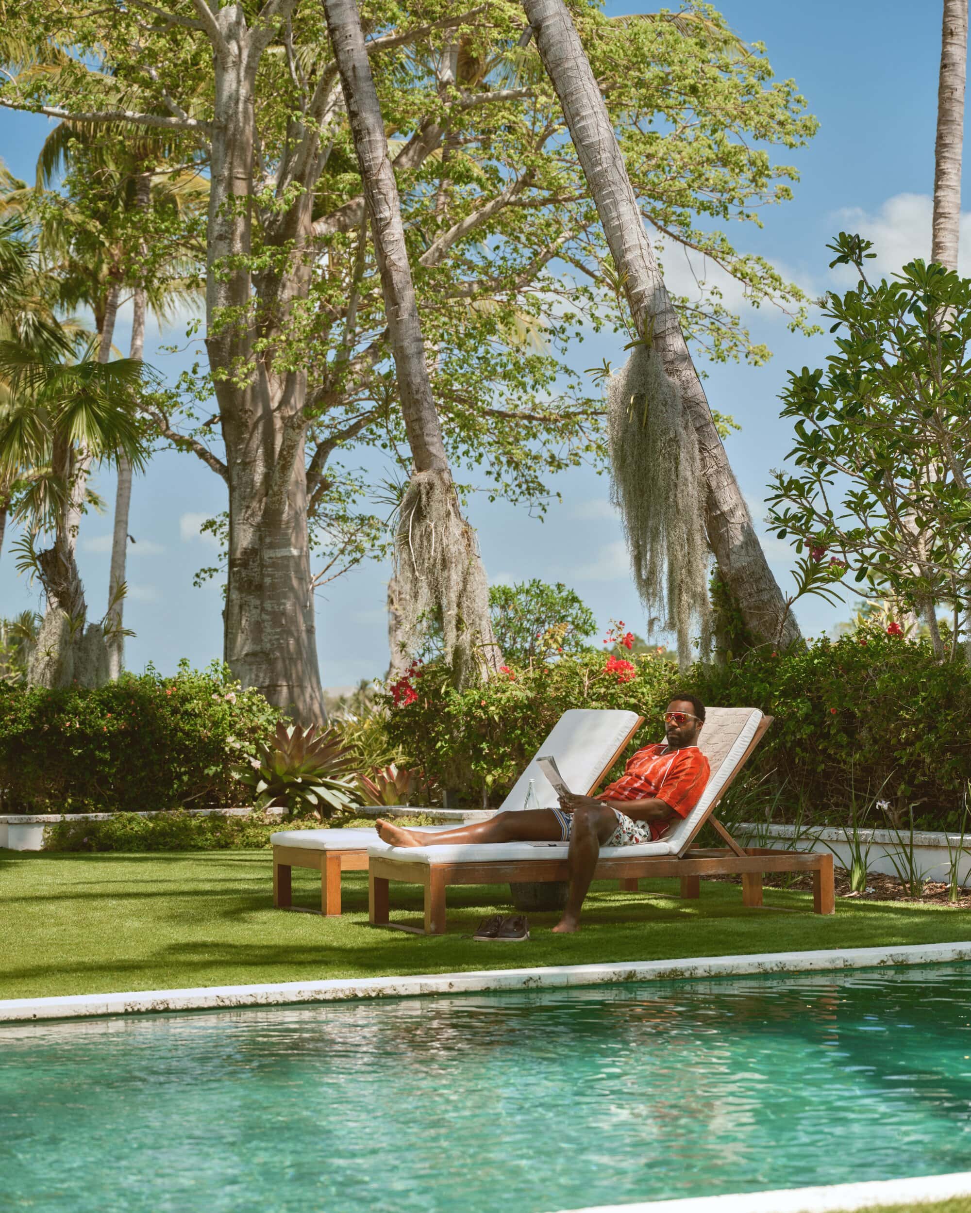 Tramell Tillman lounging on a sunbed by a pool in a tropical setting for Kith Spring 2025 campaign.