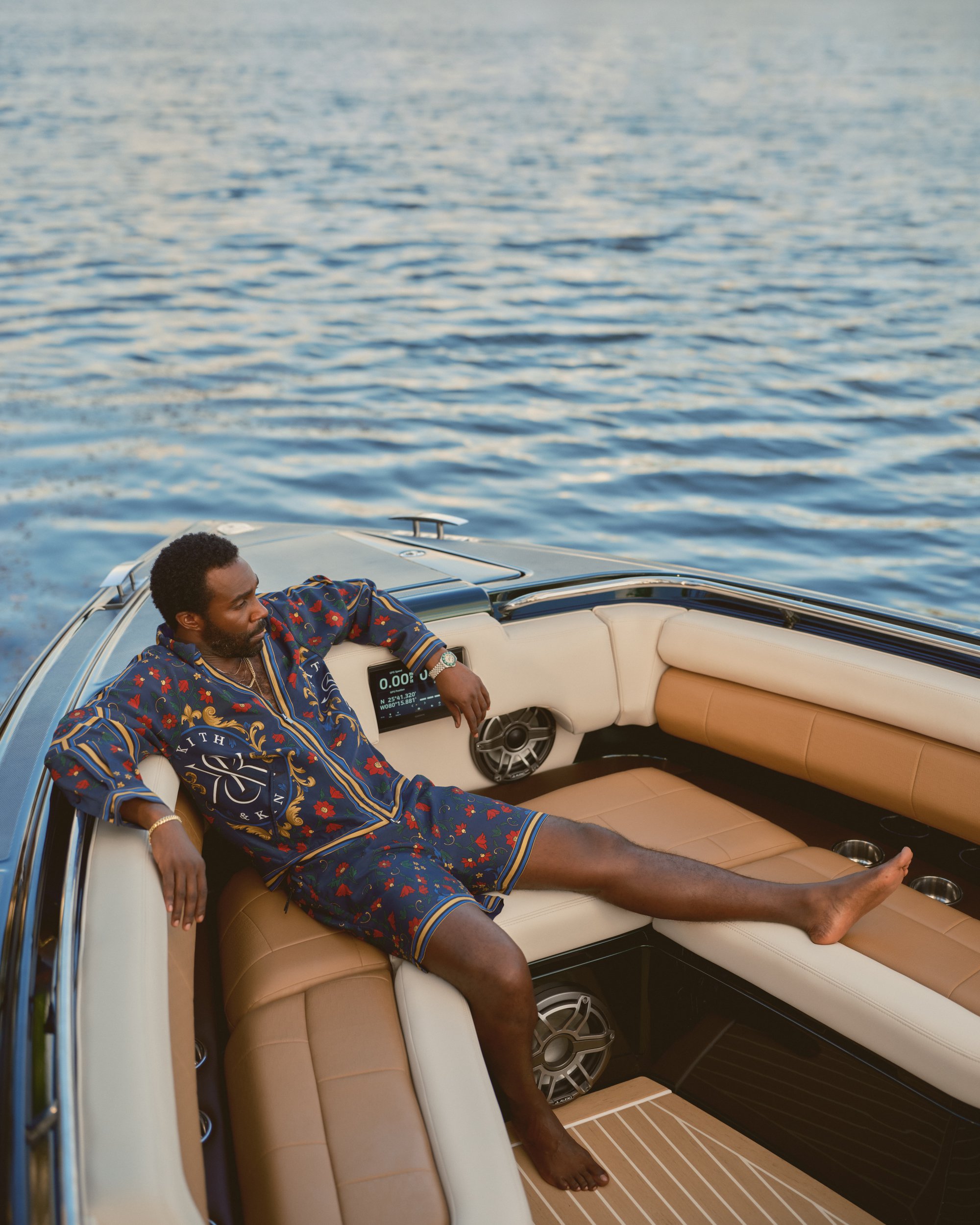 Tramell Tillman seated on a luxury boat wearing printed blue leisurewear for Kith Spring 2025 ad campaign.